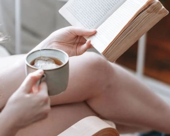 a woman reading a book and holding a cup of coffee