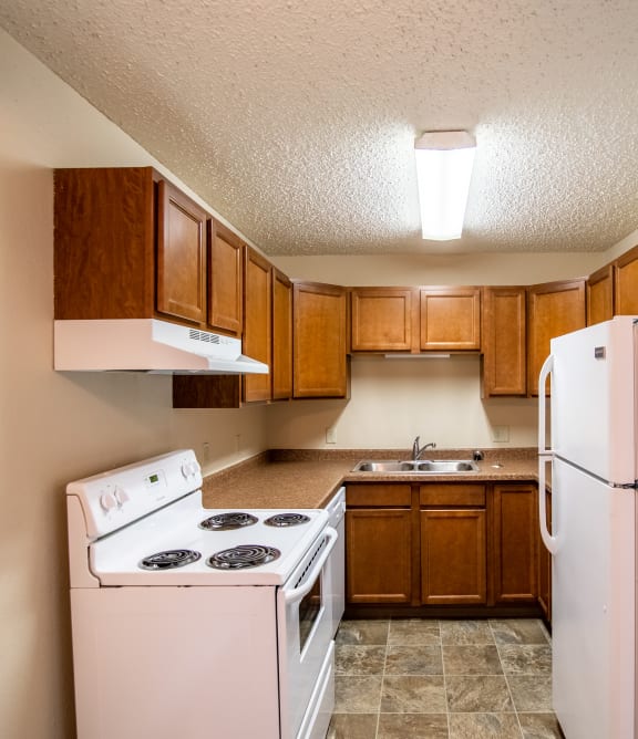 Bismarck, ND Eastbrook Apartments |a kitchen with white appliances and wooden cabinets and a refrigerator Bismarck, ND Eastbrook Apartments |a kitchen with white appliances and wooden cabinets and a refrigerator