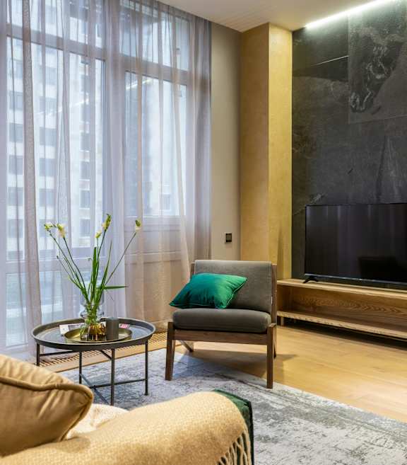 A living room with a couch, a chair, a coffee table, a TV, and a plant.