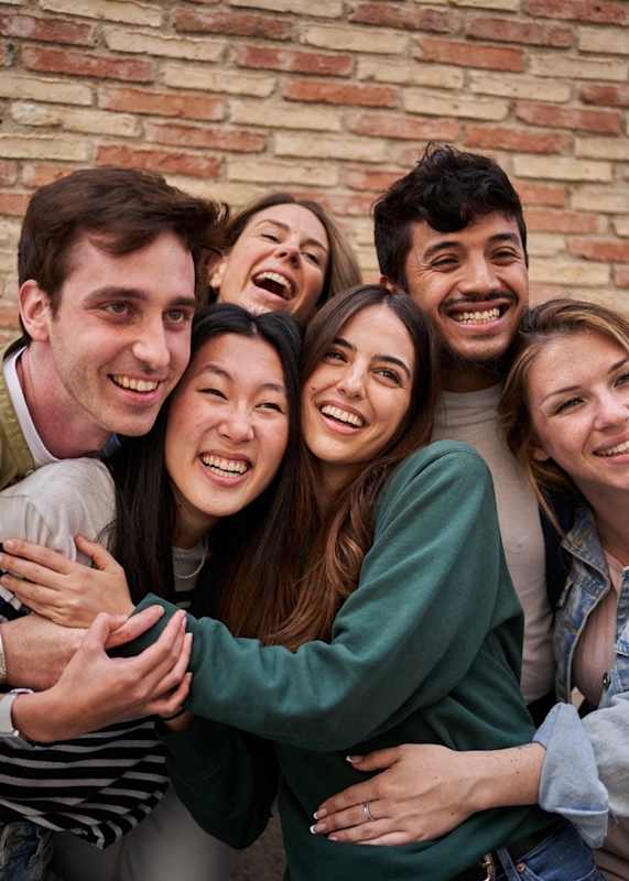 A group of people hugging each other in front of a brick wall.