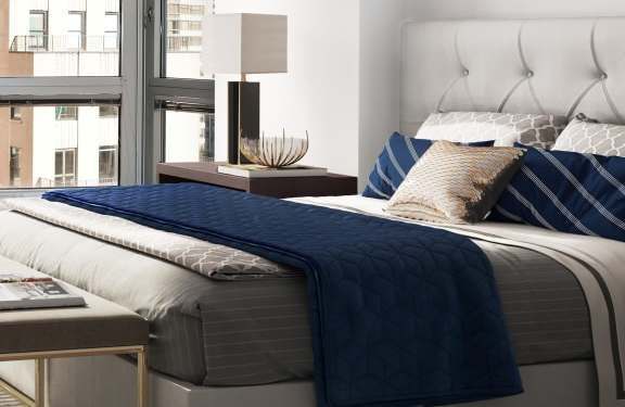 A bed with a white headboard and blue bedding is in a room with a window.
