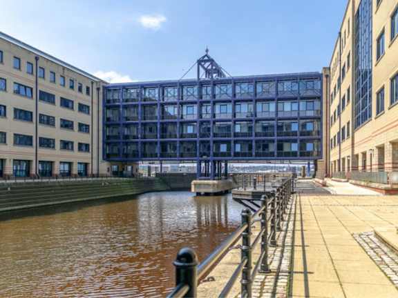 a boardwalk next to a river between two buildings at The Keel Apartments, Liverpool, L3 4GE