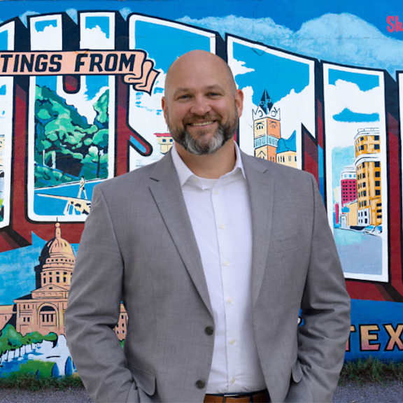 A man in a grey suit stands in front of a graffiti wall.