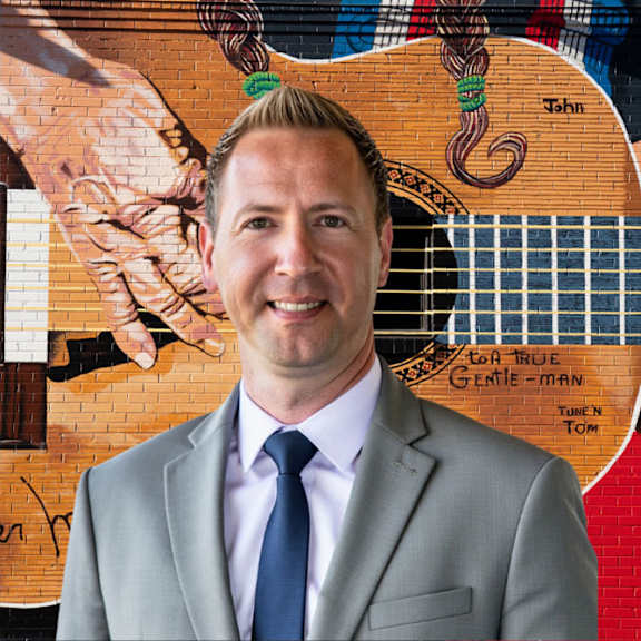 A man in a suit stands in front of a guitar.