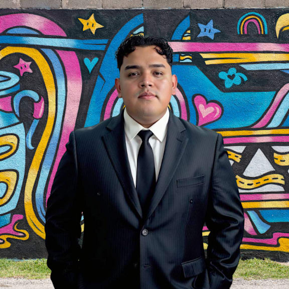 A man in a suit stands in front of a colorful graffiti wall.