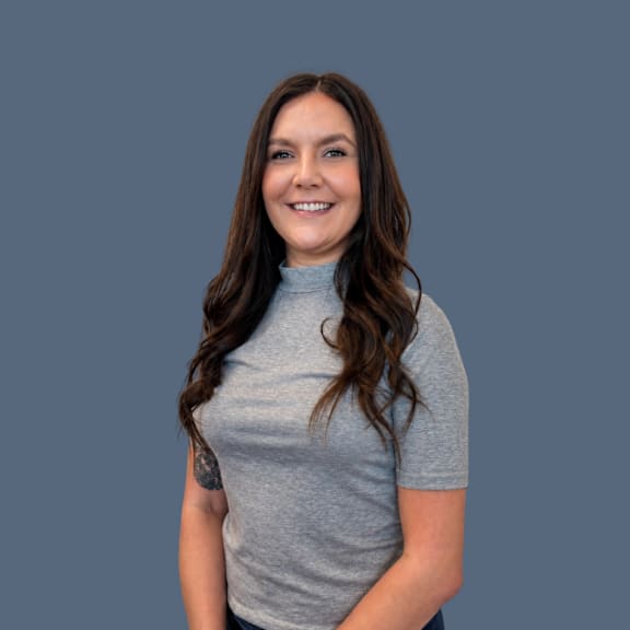 A woman with a tattoo on her left arm is wearing a grey turtleneck top.