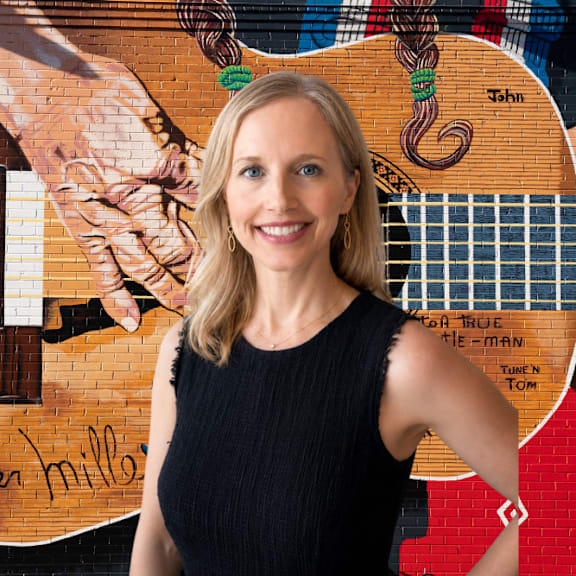 A woman in a black top stands in front of a guitar.