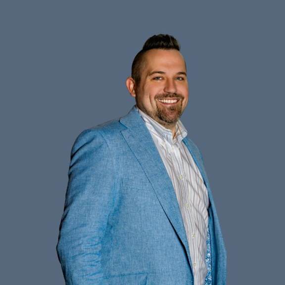 A man with a beard is wearing a blue jacket and a striped shirt.