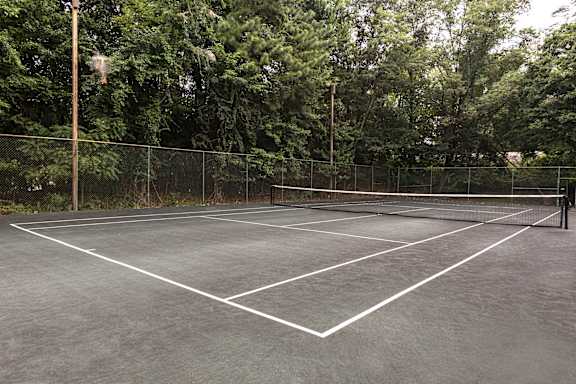 A tennis court surrounded by a fence and trees at The Brittany Apartments, Maryland
