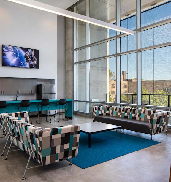 A conference room with a long table and chairs, a television on the wall, and a view of the outside through large windows.
