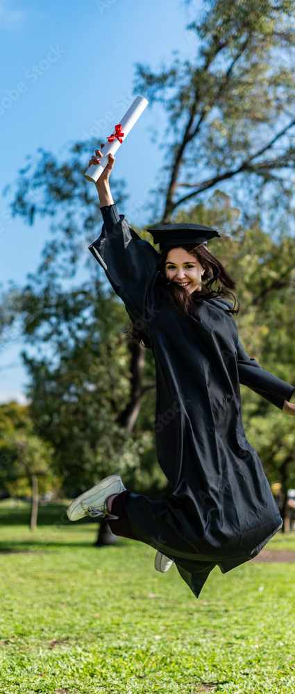 A person in graduation attire is jumping in the air with a diploma.
