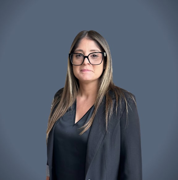 A woman with glasses and a black top is standing against a grey background.