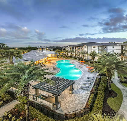 A swimming pool surrounded by palm trees and a patio area with a table and chairs.