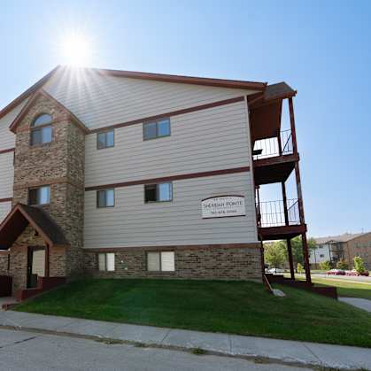 An exterior view of an apartment complex with a sidewalk in front of it. Fargo, ND Sheridan Pointe Apartments.