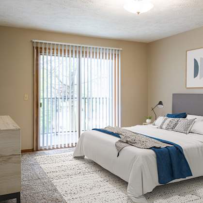 Omaha, NE Woodland Pines |a bedroom with a bed and a sliding glass door