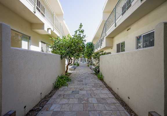 the walkway between the apartments is lined with trees and plants