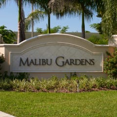 a sign for malibu gardens in front of palm trees