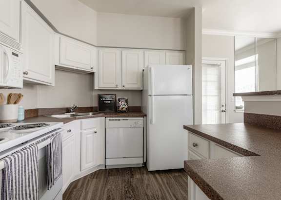 A white refrigerator is in the middle of a kitchen with white cabinets.