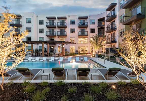 A pool surrounded by chairs and trees in front of a building.
