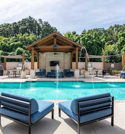 A pool with a wooden pavilion and lounge chairs.