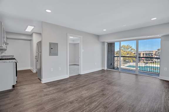 A spacious room with wooden flooring and a view of a pool through the sliding glass doors.