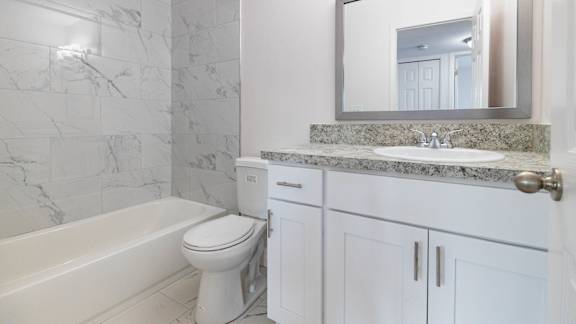 A white bathroom with a marble counter top and a large mirror.