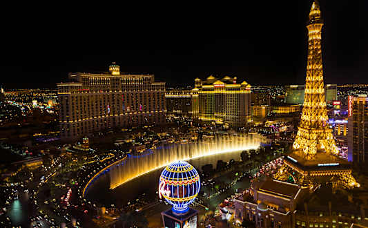 A nighttime view of a city with a large fountain and a building resembling the Eiffel Tower.
