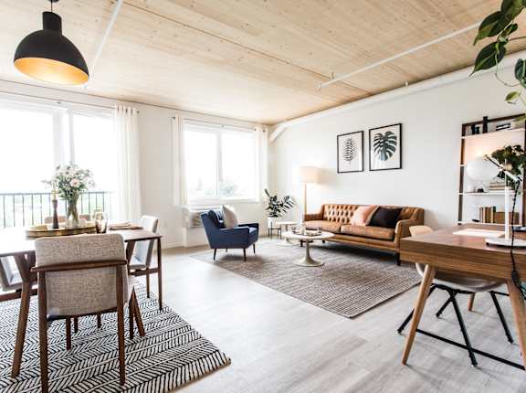 A well-lit, spacious living room with a dining table and chairs, a sofa, and a rug.