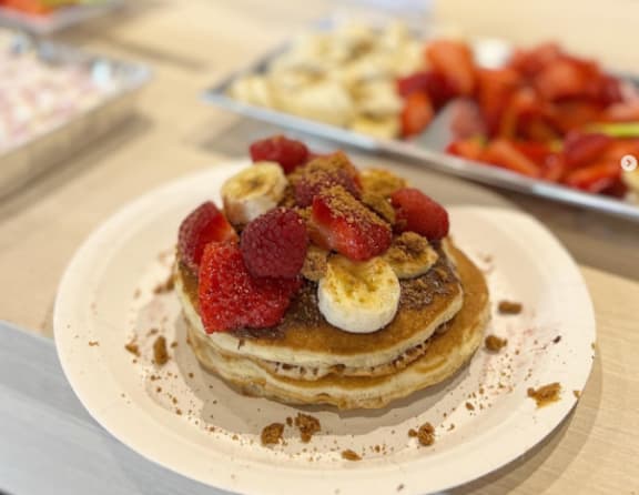 A stack of pancakes topped with banana slices, raspberries, and syrup.