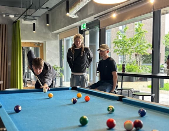 Three people playing pool in a room with a view of the outside.