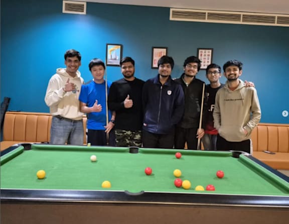A group of six men stand in front of a pool table.