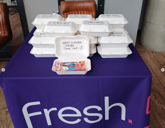 A table with a purple cloth that says fresh and white boxes of food.