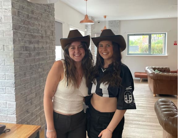 Two women wearing cowboy hats stand in a room.