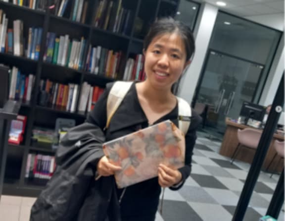 A woman in a black coat is holding a book with a colorful cover.