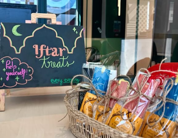 A basket of Iftar treats sits in front of a chalkboard sign.