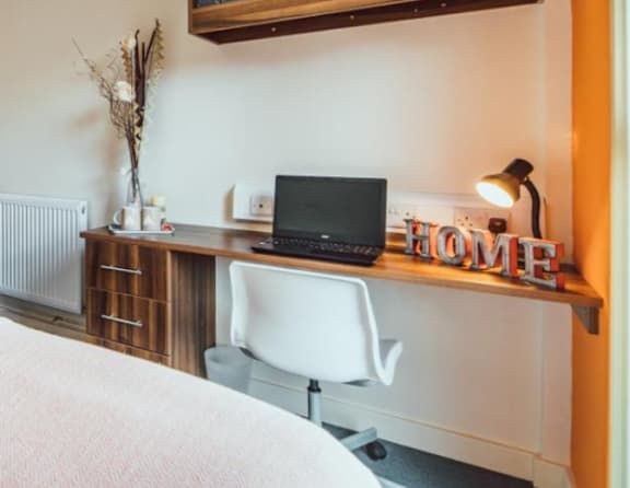 A laptop is on a desk with a white chair and a lamp.