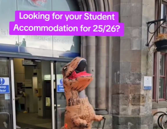 A person in a pig costume is standing in front of a building entrance.