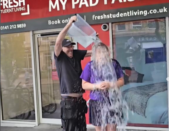 A man and a woman are playing with a large water hose outside a business.
