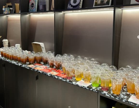 A long table is lined with glasses filled with different colored liquids.