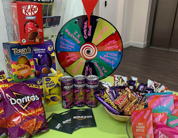A variety of snacks and drinks are displayed on a table with a wheel of fortune in the center.