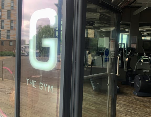 A gym with a glass door and a neon sign that says "G".