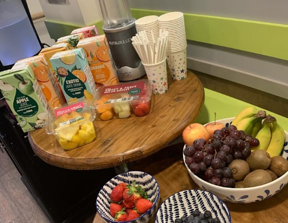 A table with a bowl of fruit, a juicer, and juice boxes.