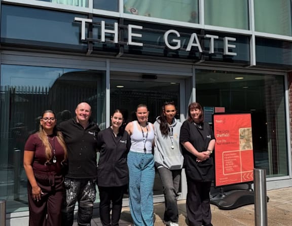 A group of people stand in front of a glass door with the word "THE GATE" written above it.