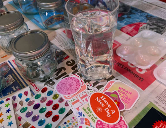 A glass of water sits on a table surrounded by various crafting materials.