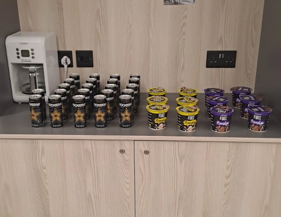 A row of jars with a yellow star on them are on a shelf next to a coffee maker.