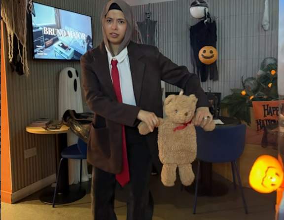 A person in a suit holding a teddy bear in front of a TV screen.