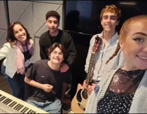 A group of five people are standing together, with one person holding a guitar.