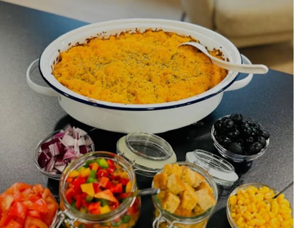 A dish of food is surrounded by small bowls of vegetables and fruits.