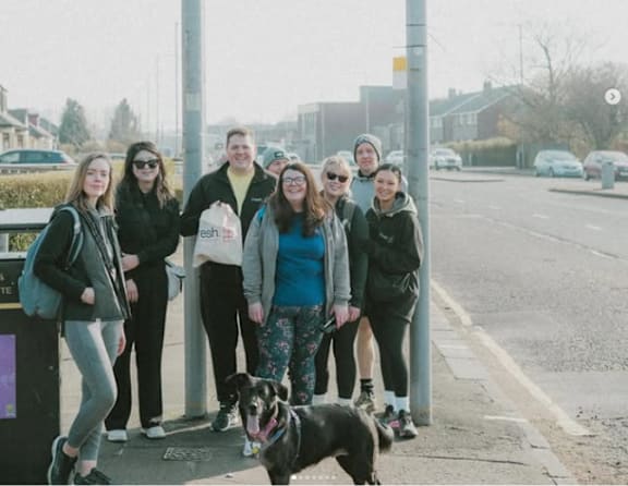 A group of people and a dog are standing on a sidewalk.