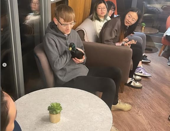 A man in a grey hoodie is sitting on a couch holding a black object.